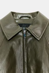 Chaqueta estilo bomber de efecto piel en color verde oliva, con cuello solapa, cierre frontal con cremallera, mangas largas y bajo elástico.