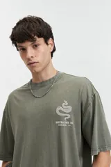 Remera oversize de algodón con efecto acid wash, color blanco hueso. Estampado grande en la espalda con un diseño circular que incluye una serpiente enroscada, texto "MISTRAL REG", "LOS ANGELES", "CALIFORNIA", "VINTAGE DENIM", "REGISTERED" y "TM 76".