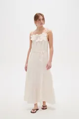 Vestido largo de algodón color blanco, con tirantes finos ajustables con lazos en los hombros, escote recto decorado con apliques florales tridimensionales, cordón ajustable en la cintura y falda larga con volados horizontales.