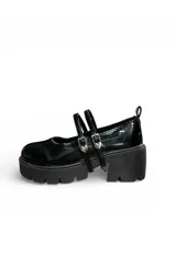 Zapato tipo Mary Jane o guillermina color negro charol, con doble tira en el empeine con hebillas metálicas en forma de corazón y suela chunky de goma con plataforma y taco ancho.