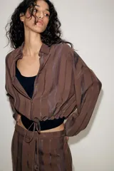 Chaqueta de cuello solapa y manga larga, confeccionada en tejido jacquard con diseño de rayas verticales. Presenta cierre frontal con botones y bajo ajustable mediante cordones.