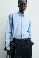 Camisa de algodón celeste con rayas verticales finas en blanco, de corte relajado (relaxed fit), cuello solapa y manga larga con puño abotonado.