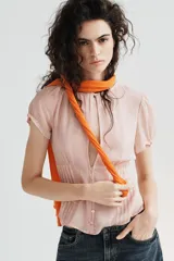 Top de georgette semitransparente color rosado, con cuello redondo, mangas cortas abullonadas y cierre frontal con botones. Presenta detalles de alforzas en la parte inferior.