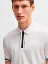 Remera polo blanca de corte regular fit, con cuello clásico y cierre de cremallera parcial. Presenta detalles de rayas en el cuello y en los puños de las mangas cortas.