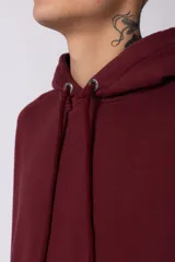 Buzo canguro color bordó con capucha y cordones ajustables. Presenta un bolsillo frontal tipo canguro y un pequeño parche rectangular con diseño gráfico en la manga derecha.