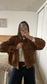 Campera tipo bomber de gamuza color camel, con diseño de doble botonadura frontal, cuello camisero y mangas largas con puños abotonados.