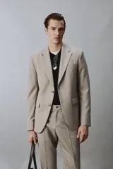 Blazer slim fit de color beige, confeccionada en tejido con lana. Presenta cuello con solapas de muesca, cierre frontal de un botón, bolsillos laterales con solapa y bolsillo de vivo en el pecho.