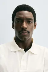 Polo de hombre color blanco hueso, de corte regular fit, con cuello solapa y tapeta de dos botones. Manga corta terminada en rib.