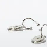 Par de aros colgantes plateados con forma de argolla y dije ovalado con borde texturizado y estrella grabada en el centro.