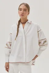 Camisa blanca de mangas largas abullonadas con bordados combinados y guardas, además de delicados bordados en el cuello y el bajo.