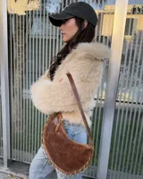 Cartera de cuero vacuno color marrón con diseño semicircular, detalle de argollas metálicas en el borde inferior y correa larga ajustable.