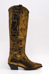 Bota alta estilo cowboy color dorado metalizado, con bordados decorativos y puntera en punta.
