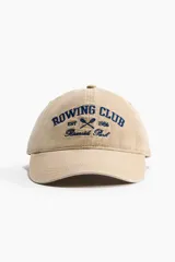 Gorra de sarga de algodón en color beige con efecto lavado, visera curva y diseño bordado en azul marino en el frente con el texto 'Rowing Club Est 1986 Riverside Park'.
