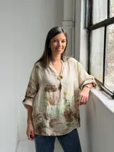 Blusa beige de lino con estampado floral en tonos marrones y verdes, escote en V con botón dorado decorativo y mangas largas.