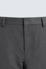 Pantalón de vestir gris oscuro, corte ancho (flare fit) y tiro alto, con bolsillos laterales y falsos bolsillos de vivo en la parte trasera. Presenta un cierre frontal con cremallera y gancho oculto, y botones a presión ocultos en el bajo.