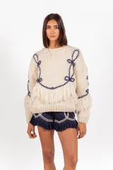 Sweater de punto 100% lana merino en color marfil, de calce holgado y cuello redondo, con detalles bordados en azul marino y flecos decorativos en el bajo y las mangas.