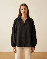 Camisa de calce amplio con cuello camisero, hombros caídos y mangas largas con puño elastizado. Presenta detalle de frunce en delantero y espalda, con cierre de botones al frente.
