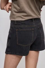 Falda short de denim con diseño a rayas verticales y costuras en contraste. Presenta frente asimétrico con efecto de falda, tiro medio, bolsillos delanteros y cierre con botón.