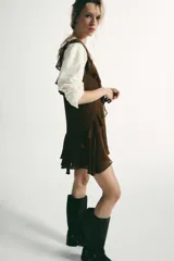 Vestido corto color marrón con escote en pico y tirantes anchos. Presenta un diseño con múltiples volantes en cascada que recorren el frente y el bajo, con un acabado asimétrico.