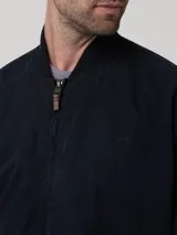 Chaqueta tipo bomber azul marino, con cuello, puños y dobladillo elásticos. Cierre frontal con cremallera y logo bordado en el pecho.