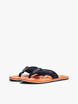 Ojotas Tommy Hilfiger con base naranja estampada con motivos florales blancos y tira de tela azul con logo de la marca.