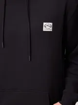 Canguro negro con capucha y cordones ajustables, con estampado gráfico en la espalda que incluye el logo de Rusty, texto "FIND YOUR SHELTER" y "ESCAPE THE NOISE", coordenadas geográficas y dibujos de plantas y árboles.