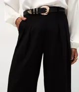 Pantalón de sastrería negro, modelo cropped de corte recto y tiro alto. Presenta pinzas frontales, bolsillos traseros y se incluye un cinturón de cuero sintético con hebilla metálica.