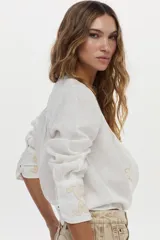 Camisa blanca de lino con cuello mao, manga larga y delicados bordados en tono tostado en el pecho y los puños.