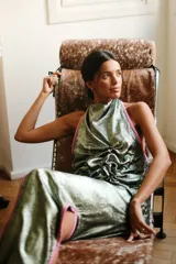 Top con escote halter de tela satinada iridiscente en tonos verdes y azules, con detalles de vivos en color rojo. Presenta jaretas frontales que aportan textura y volumen, con espalda abierta y ajuste mediante tiras para anudar.