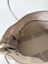 Bolso grande de cuero marrón con textura tipo cocodrilo, estructura rígida y asas para llevar al hombro. Tiene una tira con tachas y hebillas en cada extremo, también lleva lazos en los costados.