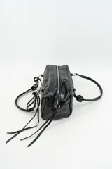 Bolso de mano tipo bowling de cuero sintético negro, con diseño estructurado, costuras decorativas y detalles de tiras largas en los laterales. Cuenta con asas cortas trenzadas con argollas metálicas.