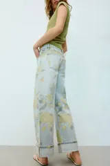 Jeans de tiro bajo y corte holgado, color celeste con estampado floral en tonos amarillos y verdes. Presenta diseño de cinco bolsillos, trabillas para cinturón y dobladillo con vuelta en los bajos. Cierre frontal con cremallera y botón metálico.