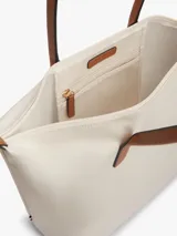 Cartera tote Tommy Hilfiger de nailon color beige, con dos asas superiores de cuero sintético tostado y cierre de cremallera. Presenta el monograma metálico TH en la parte delantera.