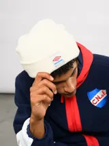 Gorro tipo beanie de tejido de punto color blanco crema, con parche frontal que incluye el logo de Umbro y la inscripción Nacional.