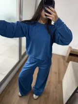 Conjunto deportivo de dos piezas color azul, compuesto por un buzo de cuello redondo y mangas largas, y un pantalón de corte ancho con cintura elástica. El buzo presenta un diseño reversible con costuras visibles.