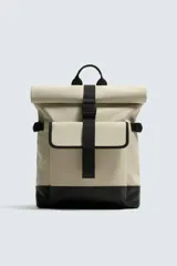 Mochila color beige con base negra, de acabado engomado. Tiene un compartimento principal con cierre de solapa con cremallera y hebilla de liberación rápida, un bolsillo interior con cremallera y un compartimento para dispositivos electrónicos de hasta 13 pulgadas. En la parte frontal tiene un bolsillo con cierre imantado. Dispone de un asa de mano y dos asas de hombro ajustables. La parte posterior es acolchada.