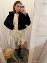 Mono corto de lino color beige, con cuello camisero, cierre frontal, mangas largas abullonadas y cinto ajustable en la cintura.