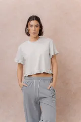 Remera crop gris claro, de calce relajado, escote redondo y manga corta, terminada con delicados volados en las mangas y en el ruedo.