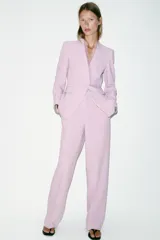 Blazer entallado color lila sin solapa, con escote en V, manga larga y bolsillos con solapa en los laterales. Presenta detalle de encaje combinado a tono en el escote y cierre frontal con un botón forrado.