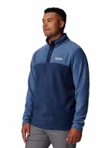 Buzo polar de media cremallera Columbia, confeccionado en tejido fleece suave y cálido. Presenta un diseño de bloques de color en tonos azul, con cuello alto y cierre frontal de botones a presión. Incluye el logo de la marca bordado en el pecho.