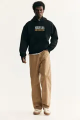 Canguro negro de mezcla de algodón con interior cepillado suave, capucha forrada y bolsillo canguro. Presenta hombros caídos y remate acanalado en puños y bajo. Estampado frontal con el logo de "Nirvana" en blanco y "Nevermind" en amarillo.