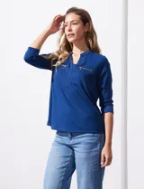 Blusa azul con cuello a la base y escote en V. Tiene bolsillos con cierre metálico.