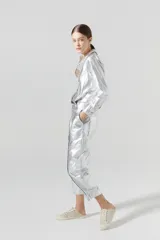 Pantalón slouchy plateado de lino orgánico con efecto metalizado y gastado. Tiene tiro medio, pinzas, cierre frontal, bolsillos laterales y traseros, y ajuste en los tobillos.