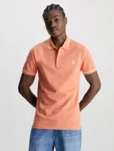 Chomba color salmón de corte slim fit, con cuello clásico y tapeta de dos botones. Presenta ribetes blancos en cuello y mangas, y logo CK bordado en blanco en el pecho.
