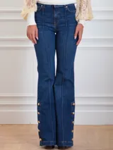Pantalón denim azul con corte flare, ajustado en el muslo y con botones metálicos dorados en el lateral exterior.