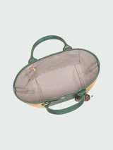 Cartera tipo crossbody de la línea Le Panier Pliage de Longchamp, confeccionada en paja trenzada con detalles en cuero blanco. Presenta un diseño pequeño con asas superiores, correa larga ajustable y extraíble, y un parche frontal con el logo de la marca. Incluye un adorno colgante con cuentas de madera.