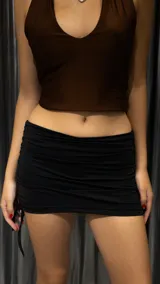 Minifalda negra de lycra con frunces laterales y cordones ajustables.