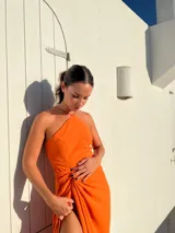 Vestido largo color naranja, con escote halter cruzado y falda tipo pareo con tajo lateral. Confeccionado en tela crepé con caída fluida.