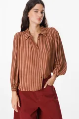 Camisa de manga larga con diseño de rayas verticales en tonos verde, azul y marrón. Presenta cuello clásico, cierre frontal con botones y mangas abullonadas con puños ajustados.