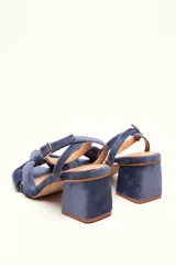 Sandalia de tacón cuadrado medio, confeccionada en terciopelo negro. Presenta un diseño de tiras cruzadas con nudo en la parte delantera y una tira ajustable con hebilla en el tobillo.